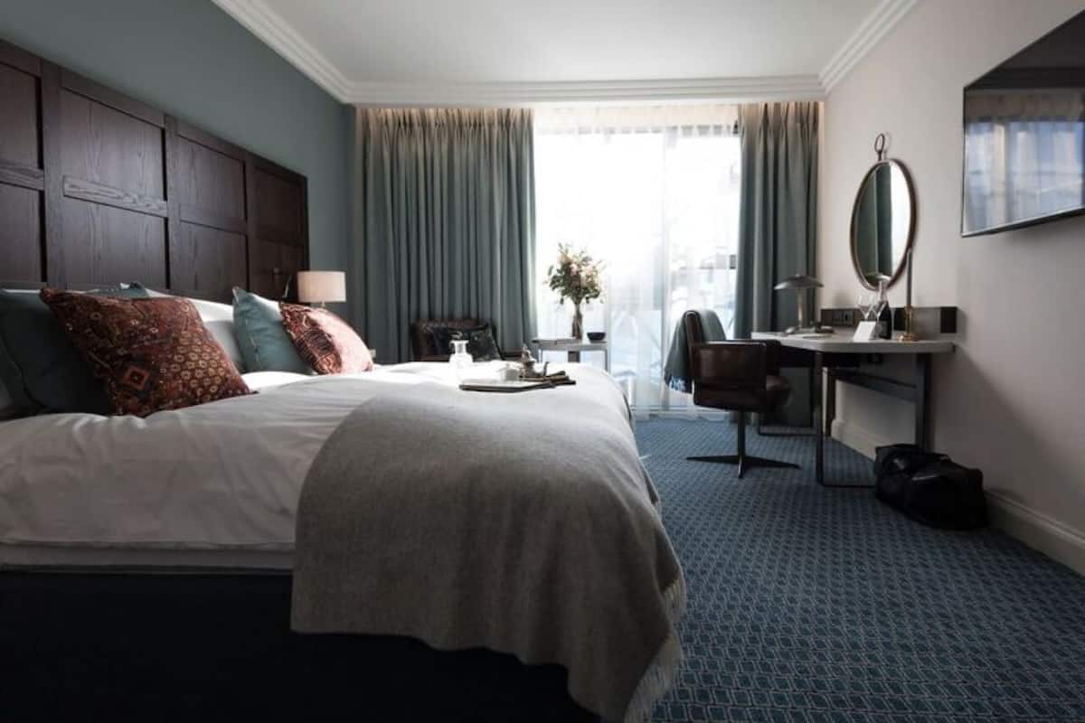A hotel room with a large bed, a desk, a chair, a mirror, and a window with curtains.