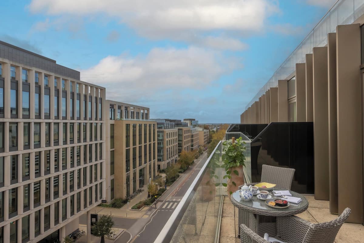 A balcony with a table set for tea, overlooking a street with modern buildings.