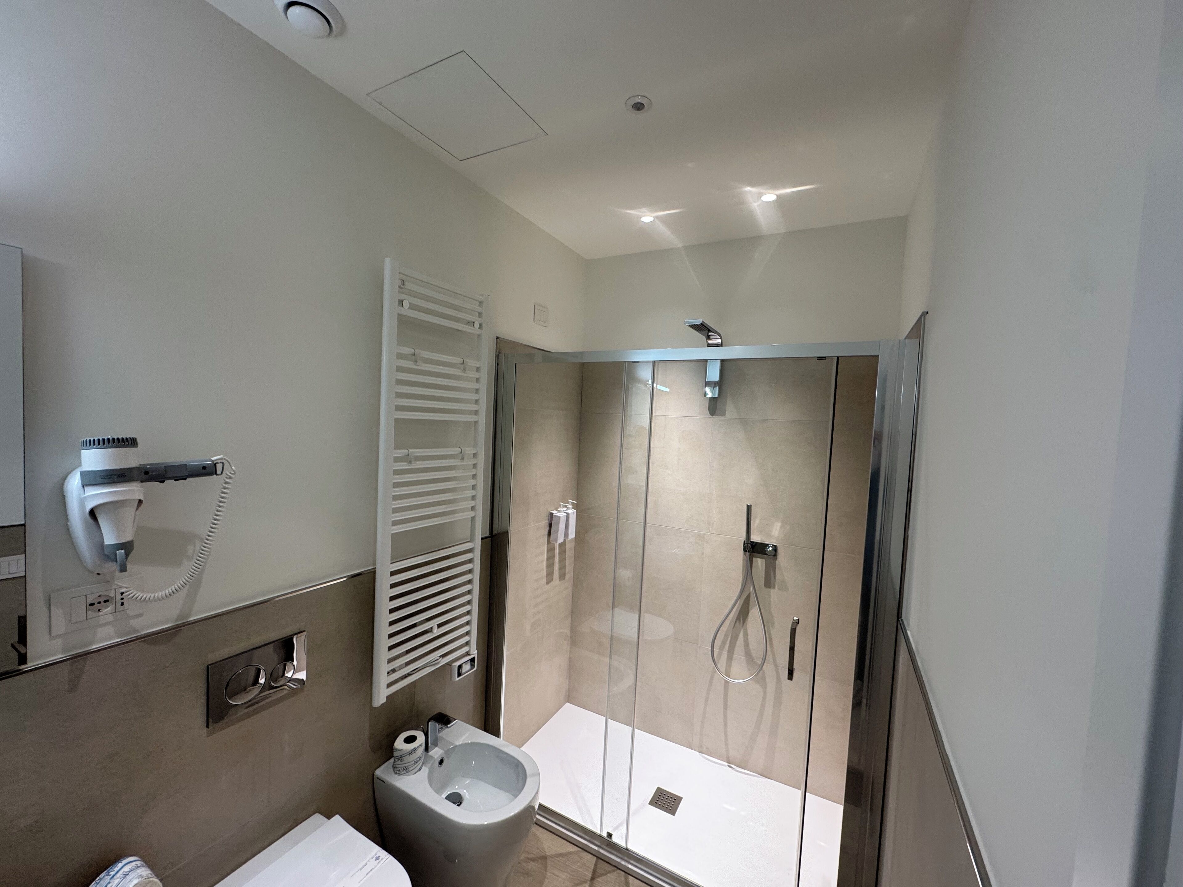 Un baño moderno con ducha acristalada, secador de pelo montado en la pared y un inodoro.