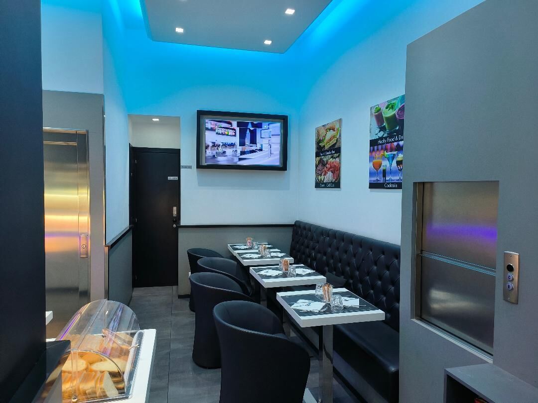Un restaurante moderno con una barra alargada, asientos tipo banqueta de cuero negro y una pantalla digital para el menú.