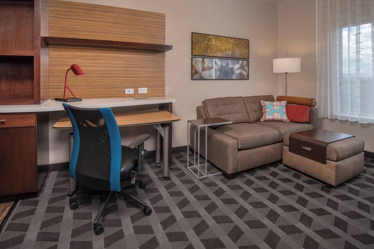 Ein Hotelzimmer mit Schreibtisch, Bürostuhl, Sofa und Ottoman.