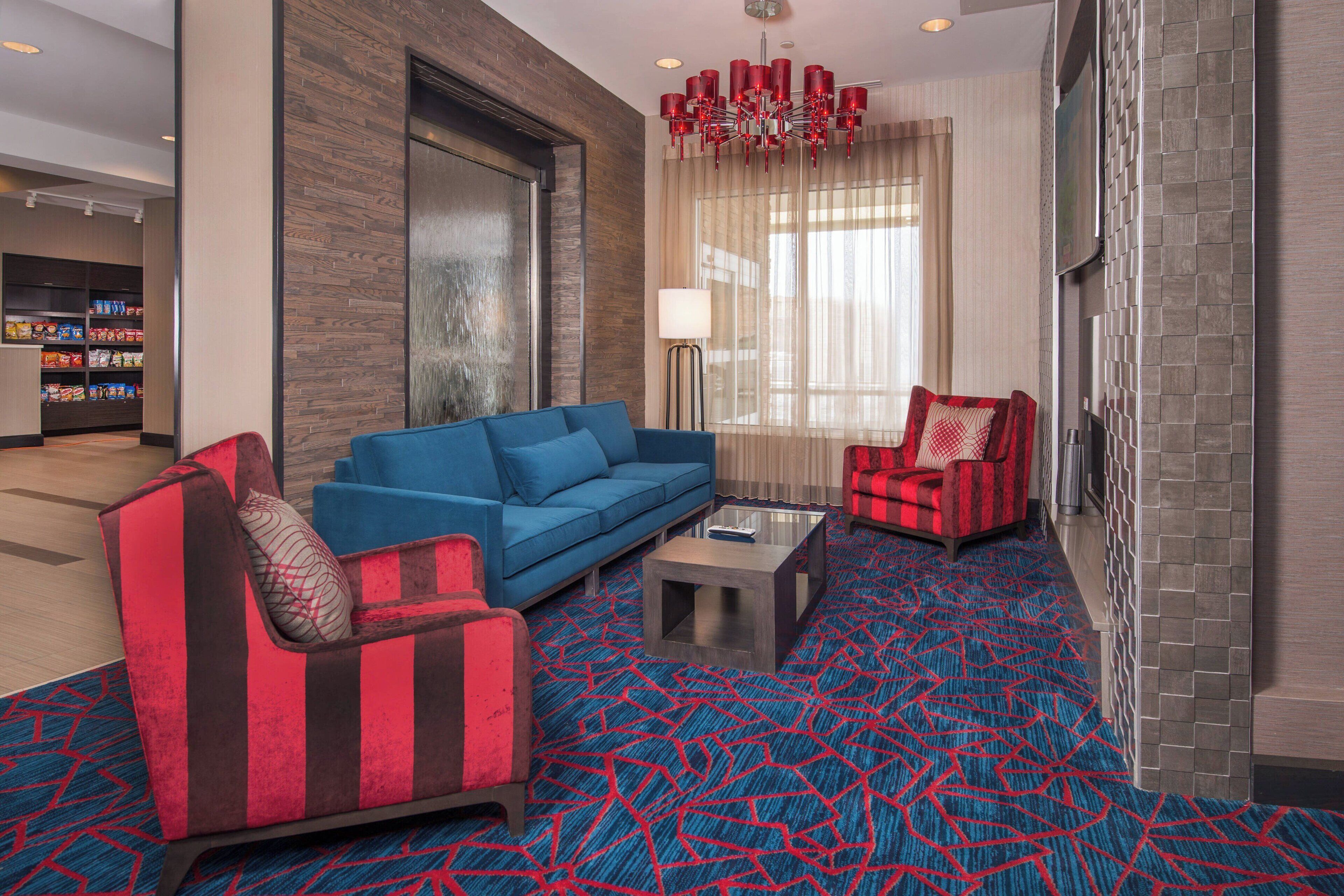 Un hall d’hôtel moderne avec un canapé bleu, un fauteuil rouge et noir, et un tapis à motifs.