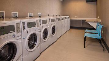 A laundry facility with multiple washing machines and a seating area with chairs.
