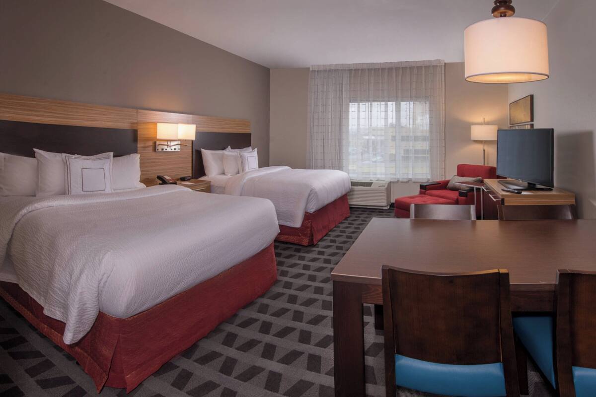Ein Hotelzimmer mit zwei Betten, einem Schreibtisch, einem Stuhl, einem Fernseher und einer Lampe.