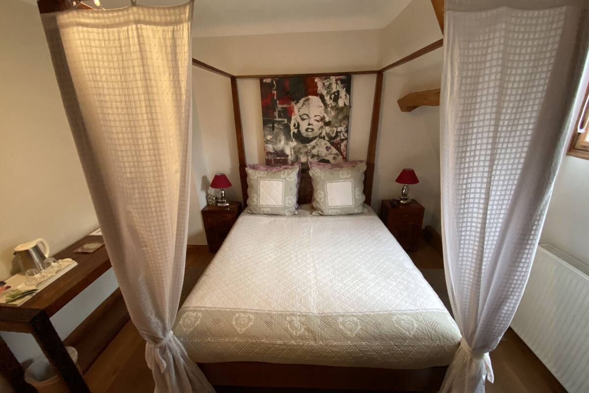 Un lit à baldaquin à quatre poteaux avec un matelas matelassé, deux tables de chevet avec des lampes et un tableau accroché au mur.