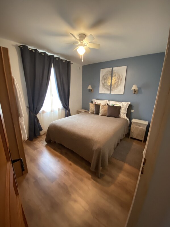 A bedroom with a bed, a ceiling fan, a nightstand, a wall-mounted lamp, and a window with curtains. - Les Plantous de Severo (Cenac-et-Saint-Julien)