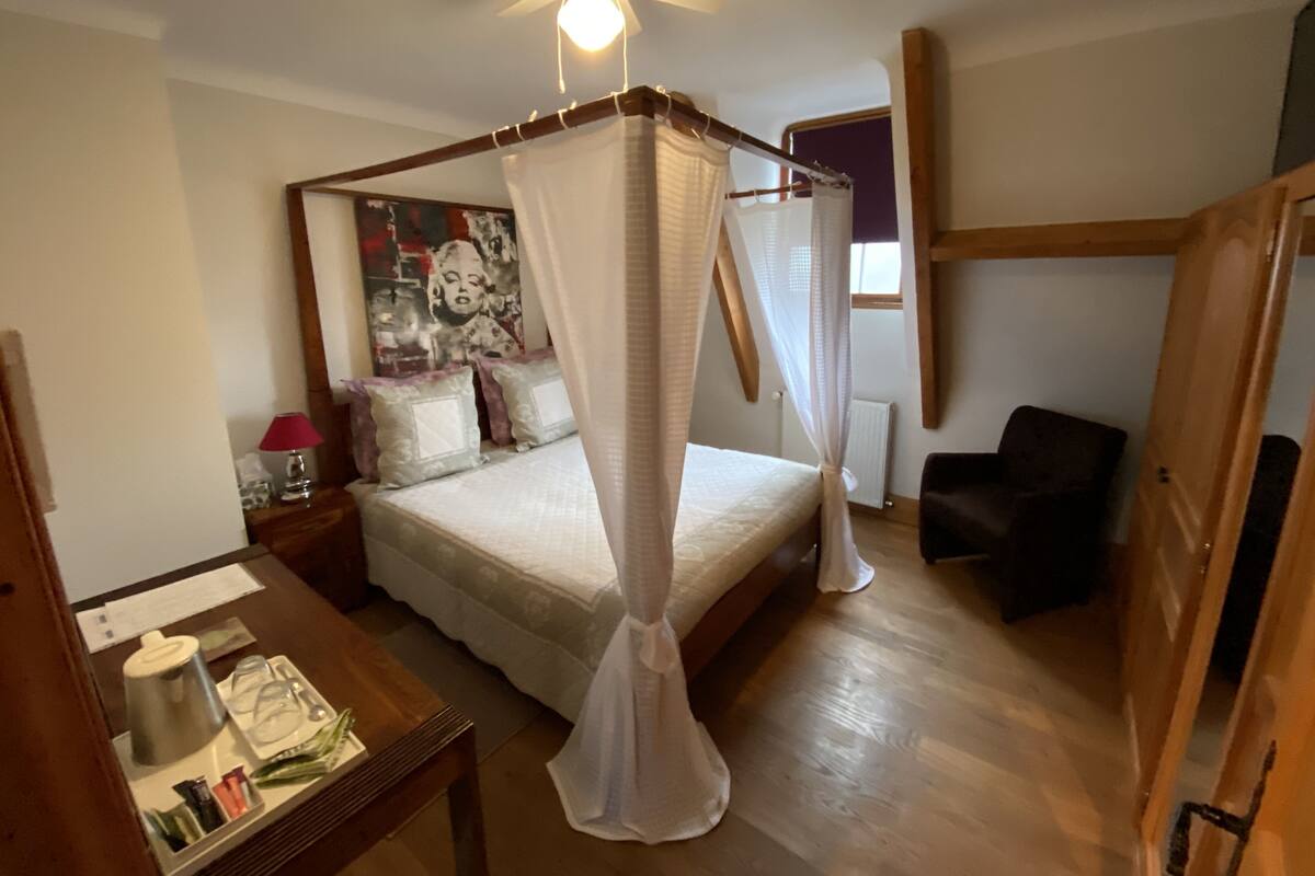 Une chambre à coucher avec un lit à baldaquin, un ventilateur de plafond, une table de chevet avec une lampe et une affiche accrochée au mur.
