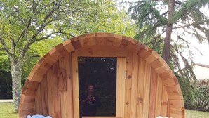 A wooden barrel-shaped structure with two seating areas, each with a cushion and a bottle of wine. - Les Plantous de Severo (Cenac-et-Saint-Julien)