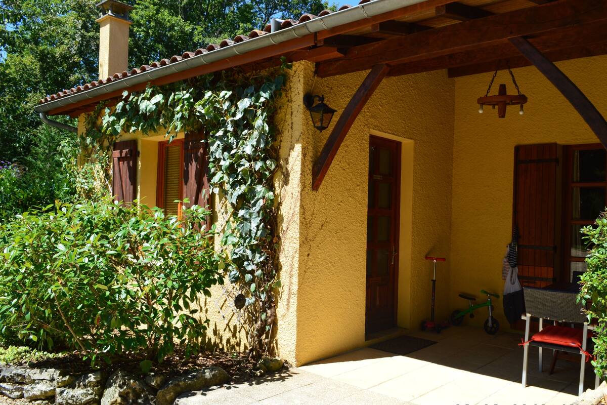 Un bâtiment jaune avec un porche en bois, une porte et une fenêtre.
