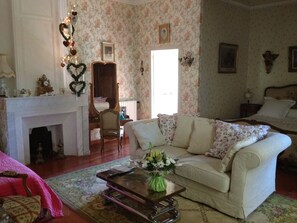 A cozy living room with a fireplace, floral wallpaper, a sofa, and a coffee table with a vase of flowers. - Domaine le Clos du Pavillon (Brignoles)