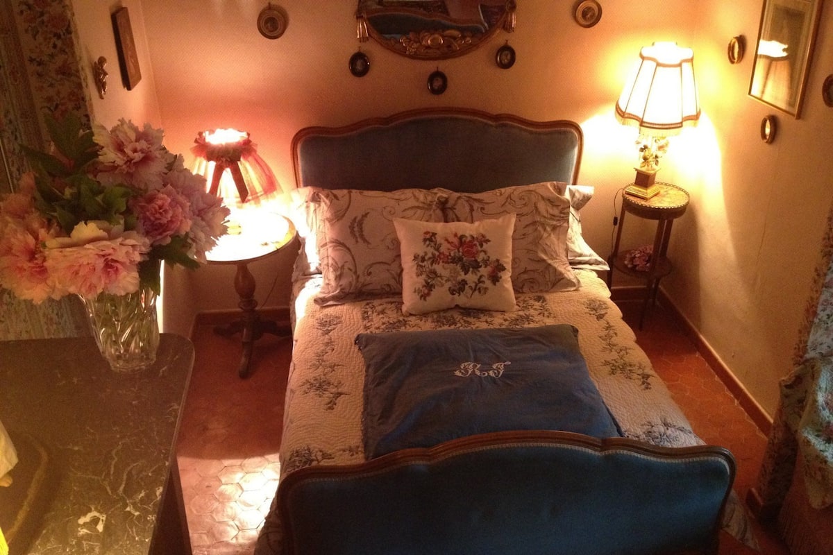 Ein Schlafzimmer mit einem Bett, Blumenbettwäsche, einer Blumenvase, einer Lampe und einem Spiegel an der Wand.