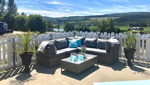 An outdoor patio with a sofa and coffee table, surrounded by a white picket fence, overlooking a scenic landscape. - Kongsvinger Budget Hotel (Kongsvinger)