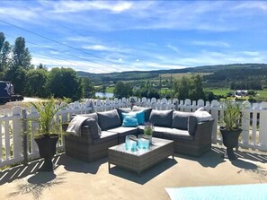 An outdoor patio with a sofa and coffee table, surrounded by a white picket fence, overlooking a scenic landscape. - Kongsvinger Budget Hotel (Kongsvinger)