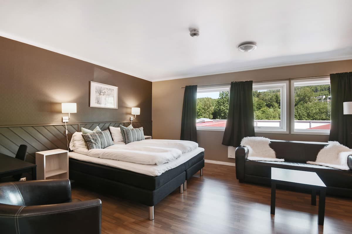 Une chambre d’hôtel moderne, dotée d’un grand lit, d’un canapé, d’un bureau et d’une fenêtre avec des rideaux.