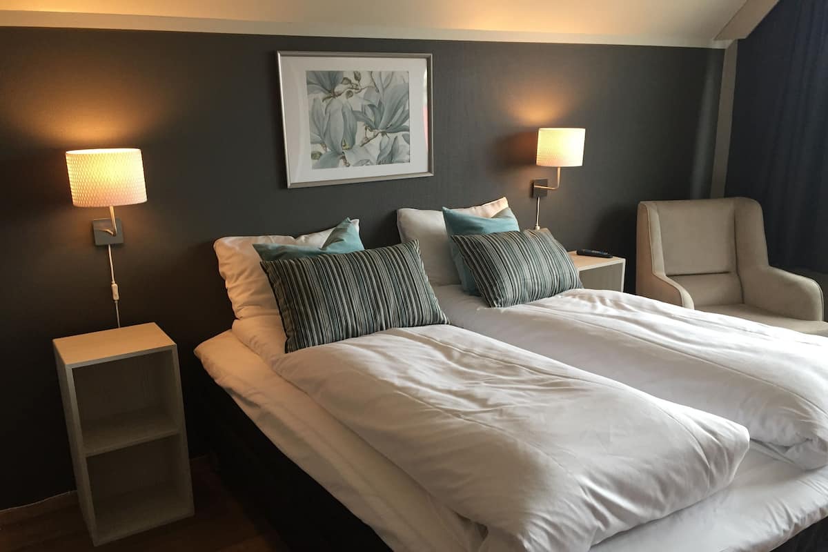 Une chambre d’hôtel avec un grand lit, deux tables de chevet, une chaise et des lampes fixées au mur.