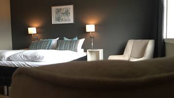 A hotel room with a bed, two bedside lamps, a chair, and a framed artwork on the wall.