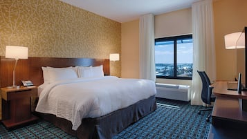 Habitación de hotel con una cama grande, dos mesitas de noche con lámparas, un escritorio con una silla y un ventanal con vistas a la ciudad.