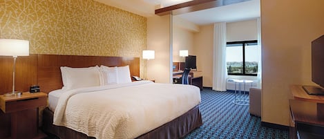 A hotel room with a large bed, a desk, a TV, and a view of the city through the window.