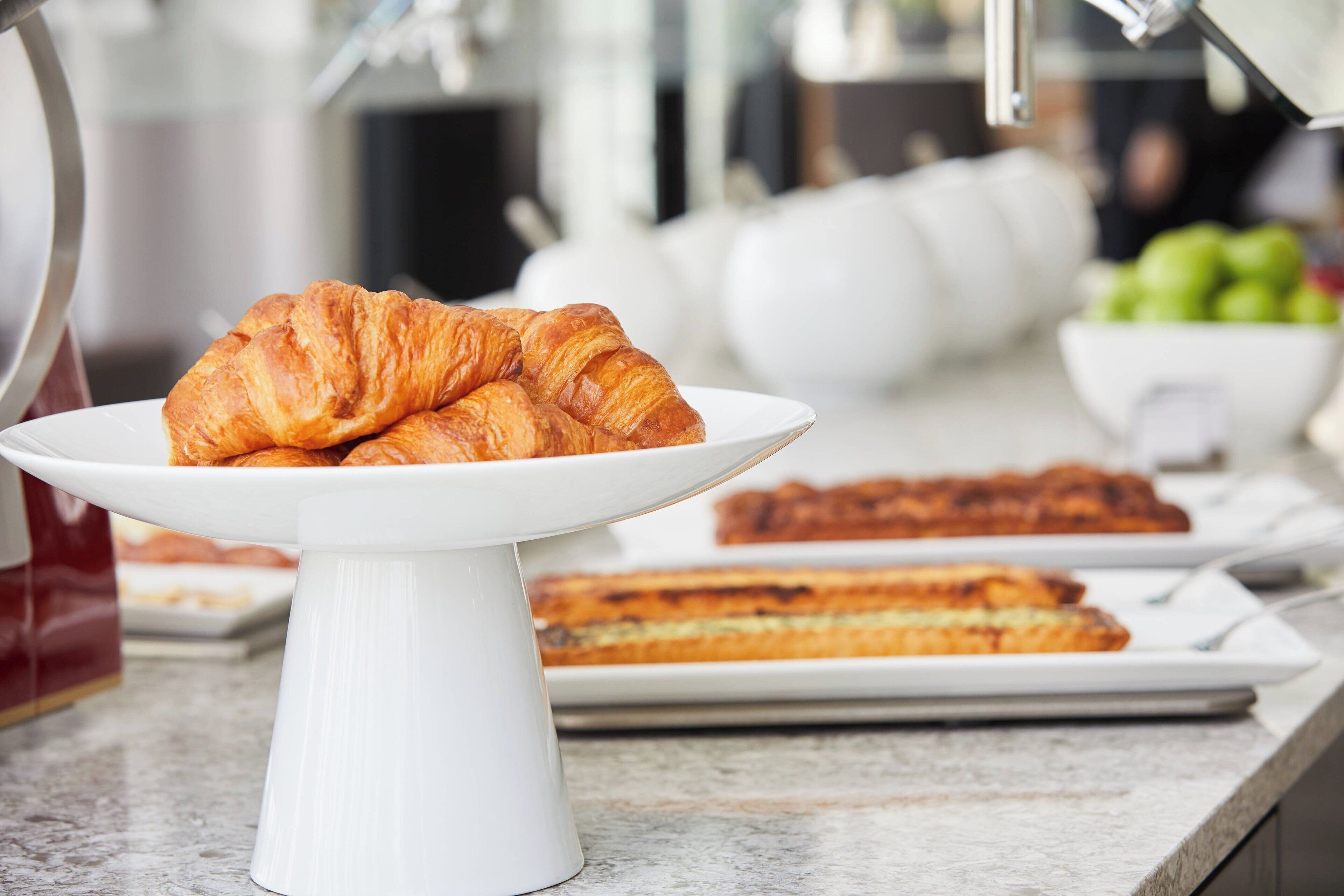 Een ontbijtbuffet met croissants en andere gebakjes op witte schalen.