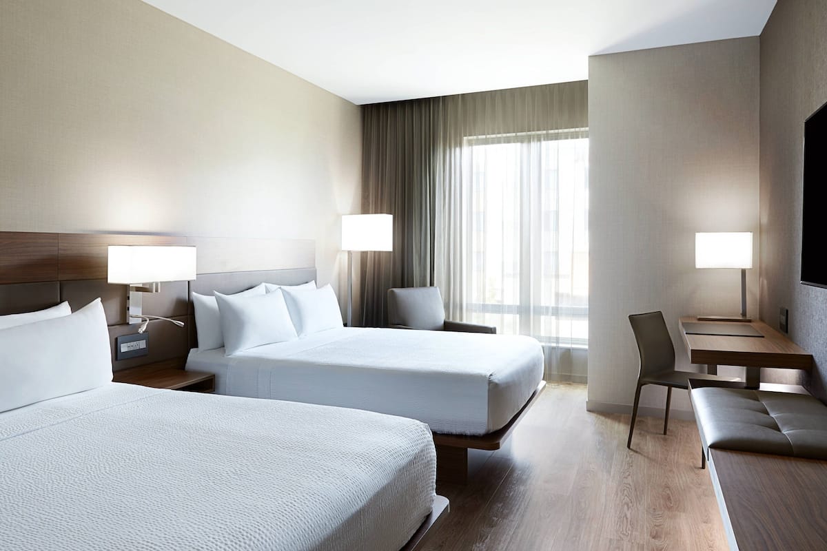 Una habitación de hotel con dos camas, un escritorio, una silla y un televisor.