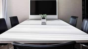 Une salle de conférence avec une grande table, des chaises noires, une plante en pot et un téléviseur à écran plat fixé au mur.