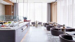 Un restaurante moderno con una barra larga, diferentes opciones de comida y una zona de estar con mesas y sillas.