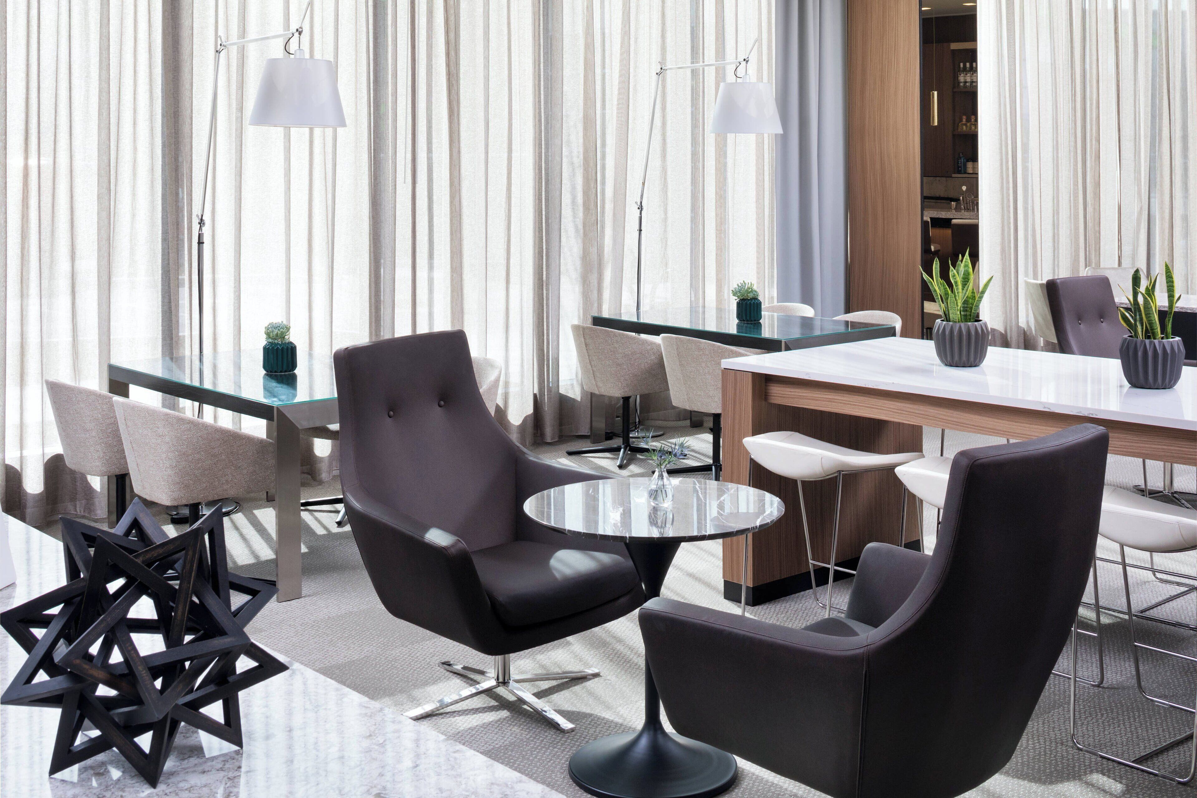 A modern hotel lobby with a glass coffee table, black upholstered chairs, and a wooden reception desk.