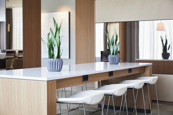Une cuisine moderne avec un plan de travail blanc, des armoires en bois et un coin bar avec des tabourets. On peut voir deux plantes en pot sur le plan de travail.