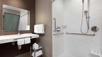 A modern bathroom with a large mirror, white sink, and a walk-in shower with grab bars.