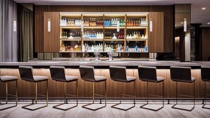 Una zona de bar con paneles de madera, varias estanterías llenas de botellas de licor y taburetes de bar.