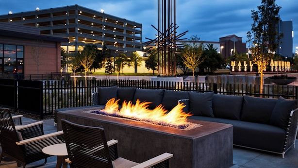 Un área de estar al aire libre con una chimenea, una valla de metal negro y un edificio al fondo.