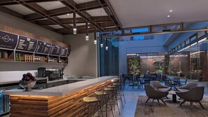 Un área de bar moderna con mostrador de madera, taburetes y una pizarra de menú.