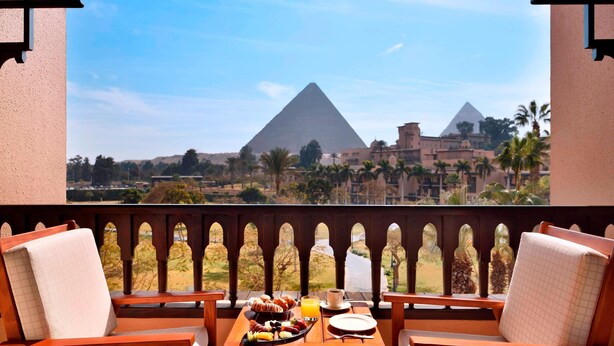 A balcony with a table set for breakfast, overlooking the pyramids. - Marriott Mena House Cairo (Giza)