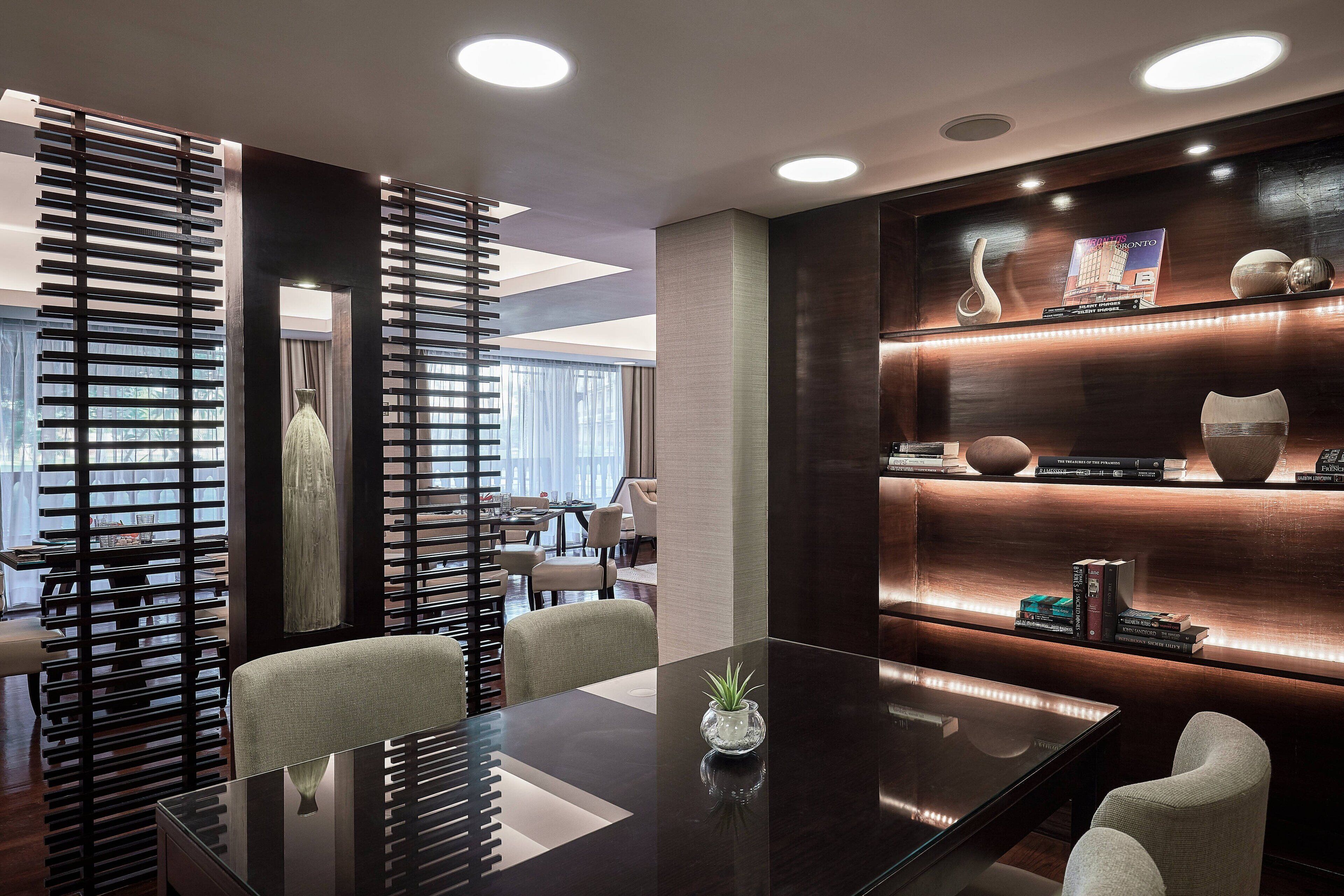 A modern conference room with a glass table, a potted plant, and a bookshelf with books and decorative items.