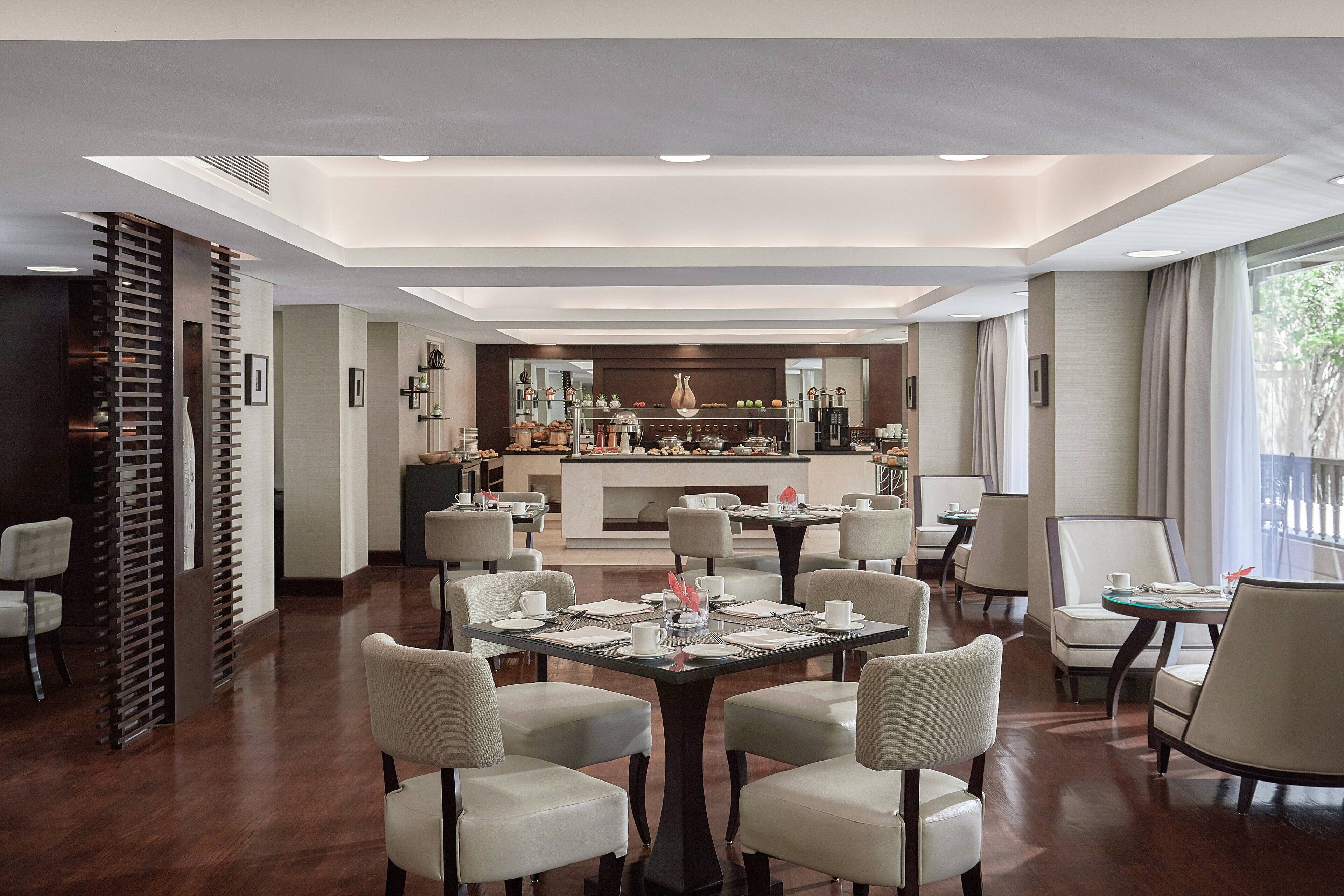 A modern hotel lobby with a bar area, multiple seating arrangements, and a view of the outdoors.