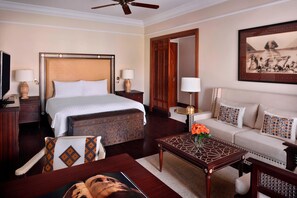 A hotel room with a large bed, a sofa, a coffee table with a vase of flowers, and a painting on the wall.