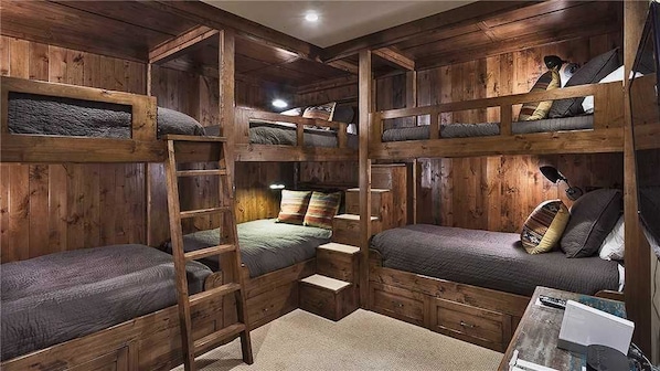 A multi-level wooden cabin with bunk beds, a ladder, and a small table with a lamp.