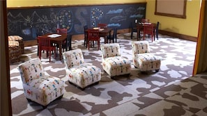 A room with patterned carpet, several chairs, a table, and a chalkboard wall with drawings.