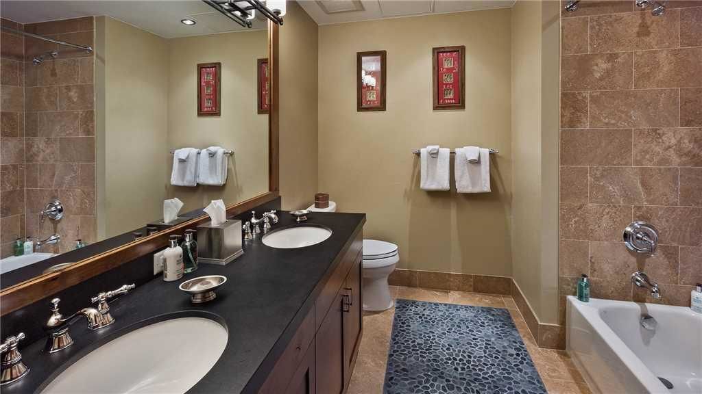 A bathroom with two sinks, a toilet, and a bathtub. There are towels hanging on the wall and a mirror above the sinks.