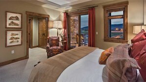 Une chambre d’hôtel avec un grand lit, une chaise, un balcon avec vue et des tableaux encadrés au mur.
