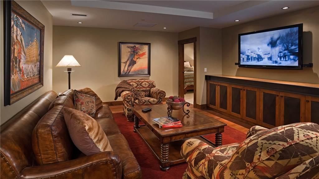 A living room with a leather sofa, patterned armchairs, a coffee table, and a flat-screen TV mounted on the wall.