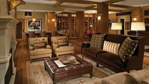 A spacious living room with a brown leather sofa, striped armchairs, and a brown ottoman. There are bookshelves in the background and a large painting on the wall.