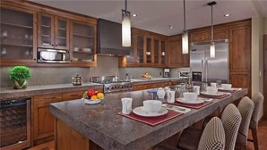 A modern kitchen with wooden cabinets, stainless steel appliances, and a long island with dining setup.