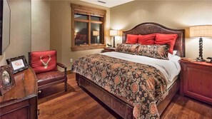 A bedroom with a large bed, a wooden chair with a red cushion, a wooden nightstand, and a window with a view. - Hahns Peak 417 4 BedroomCondo By Moving Mountains (Steamboat Springs)