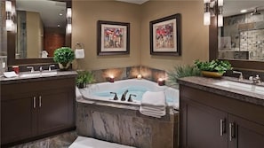 Un baño moderno con una bañera grande, dos lavamanos, armarios de madera oscura y cuadros enmarcados en las paredes.
