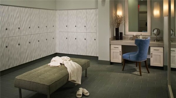 Ein Zimmer mit einer Bank, einem Stuhl, einem Schminktisch mit Spiegel und Schließfächern.