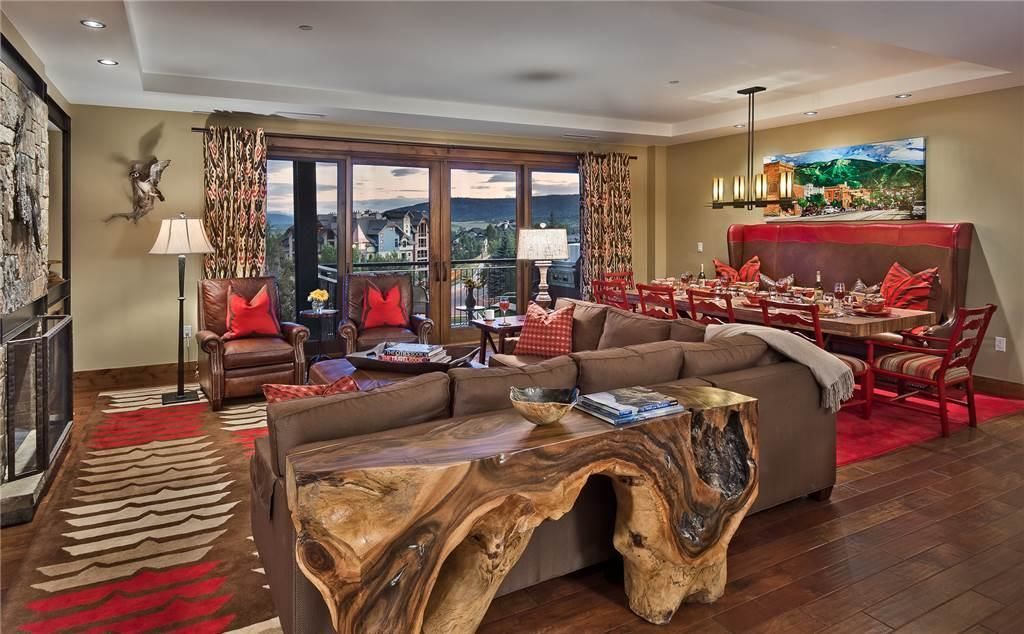 A spacious living room with a large sofa, a wooden coffee table, and a dining area with red chairs.