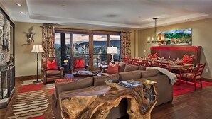 A spacious living room with a large sofa, a wooden coffee table, and a dining area with red chairs. - Zirkel Mountain 419 4 BedroomCondo By Moving Mountains (Steamboat Springs)