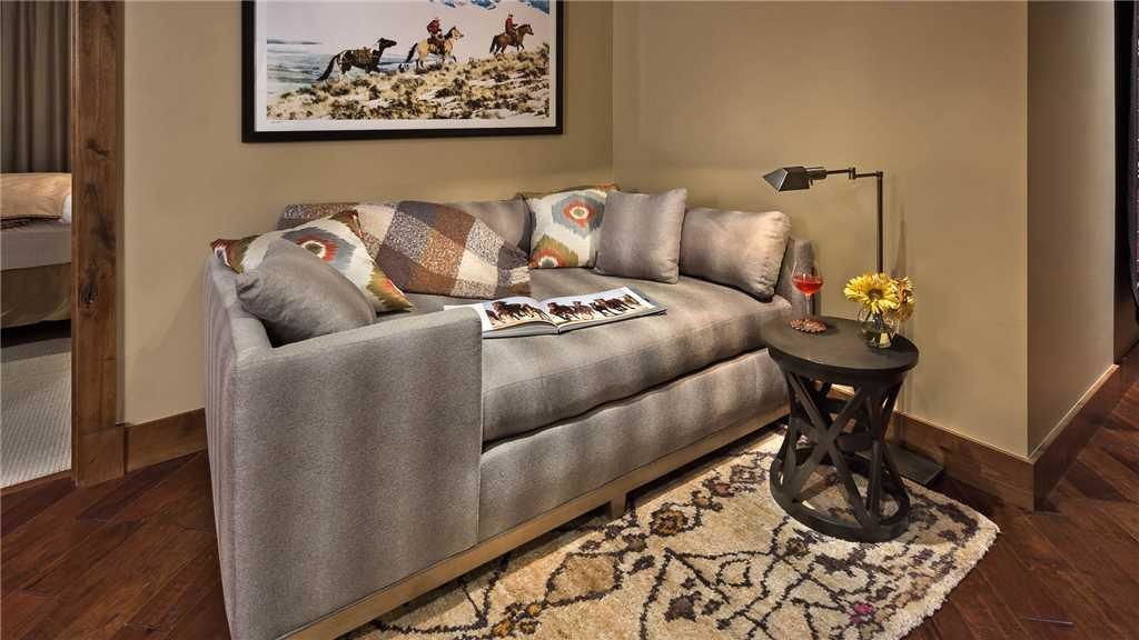 A modern living room with a grey sofa, patterned cushions, a small round table with a lamp, and a framed picture on the wall.