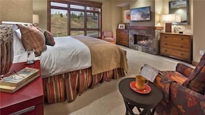 A hotel room with a bed, a desk with books, a chair, a fireplace, and a television. - Maroon Mountain 507 4 BedroomCondo By Moving Mountains (Steamboat Springs)